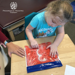 Sierra traces number "3" using a sensory gel bag over an outline.