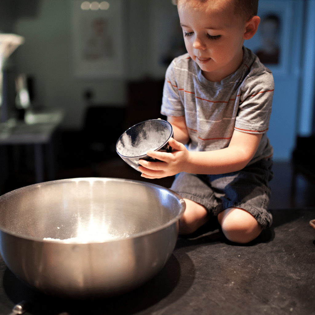 child pouring dry ingredients into a bowl.