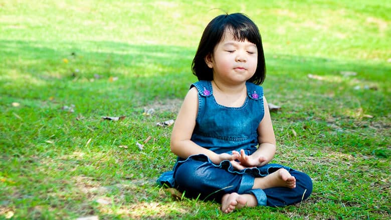 Child with eyes closed breathing in through the nose while sitting on the grass