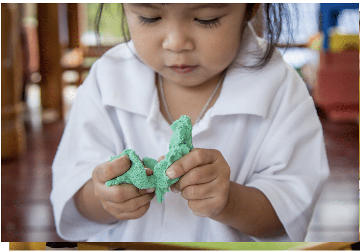 Child playing with green playdoh using both hands at midline