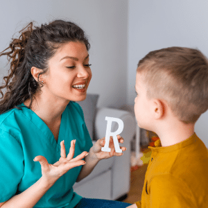 A speech therapist is holding up the letter R while working with a boy.