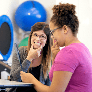 A speech therapist is smiling with a student.