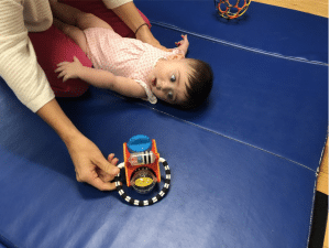 A mother uses a toy to get a child to turn to the left.